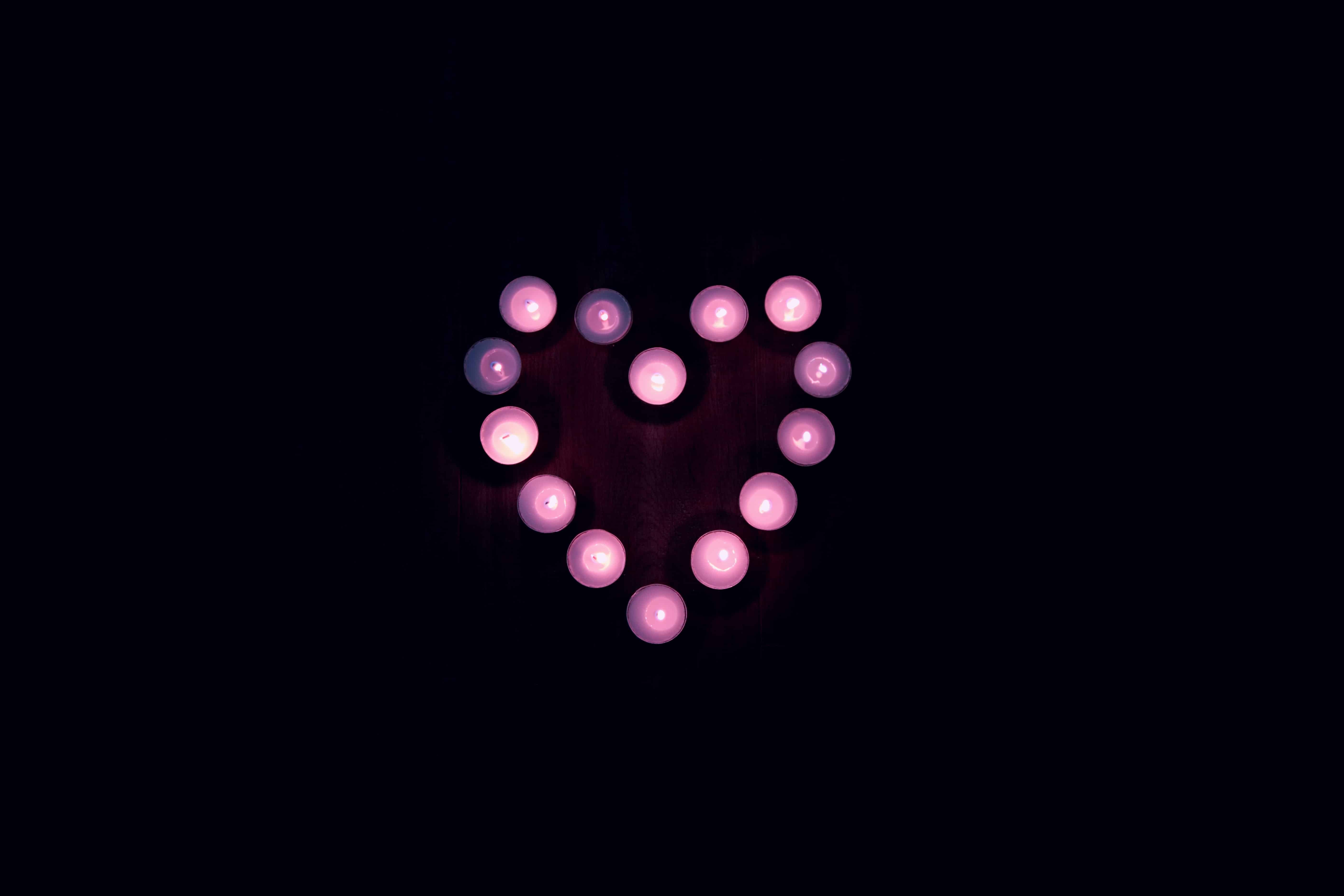 fotografia vista de cima: em uma superfície de madeira, velas roxas acesas formam a imagem de um coração 