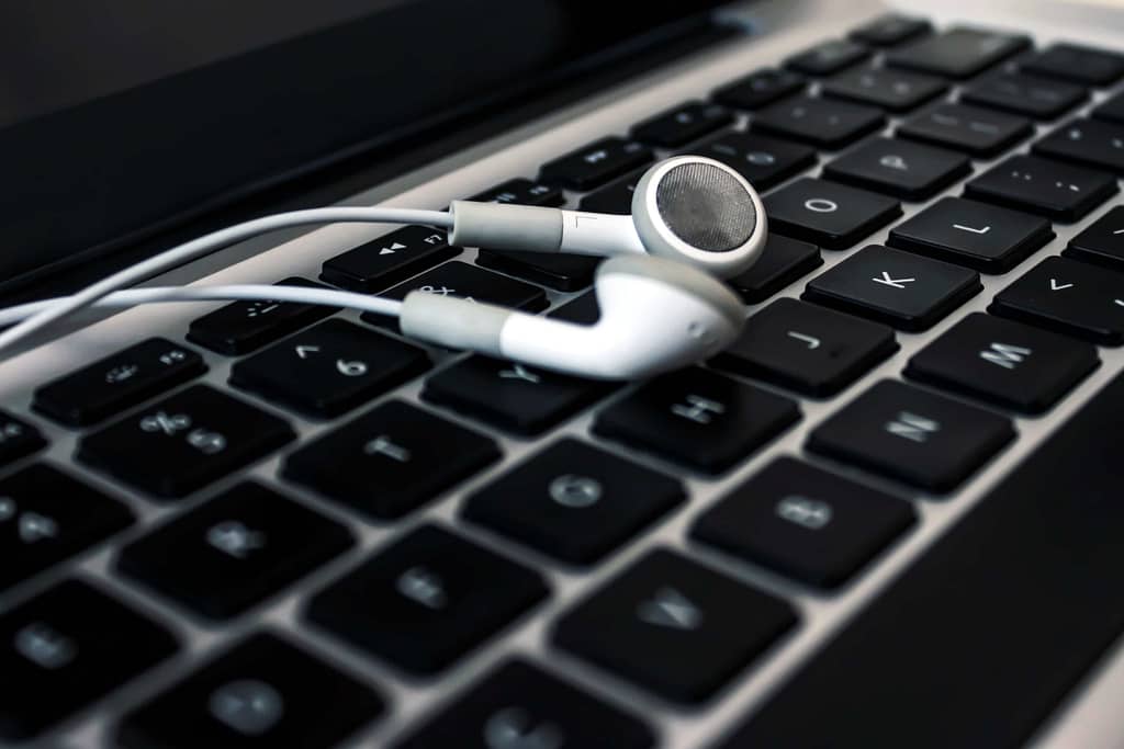 Foto de um fone de ouvido branco sobre um teclado de notebook.