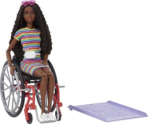 Foto da boneca Barbie Fashionista Negra Com Cadeira de Rodas. Ela é uma Barbie negra com longos cabelos ondulados, usa um óculos em formato de coração, vestido de listras horizontais coloridas, pochete branca e uma cadeira de rodas vermelha e preta. Ao lado dela há uma pequena rampa de acesso roxa de plástico.